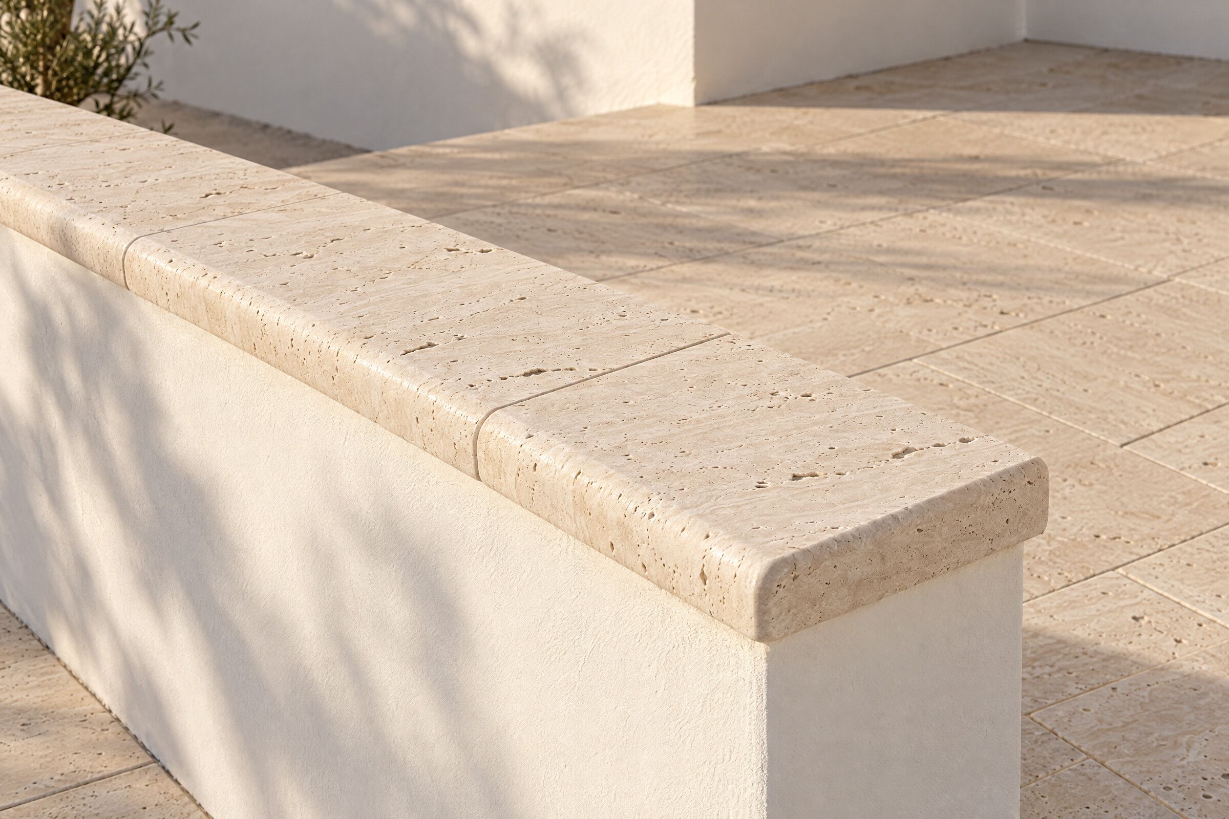 Illustration of tumbled travertine coping with a rounded edge capping a low white wall, beside a travertine patio.