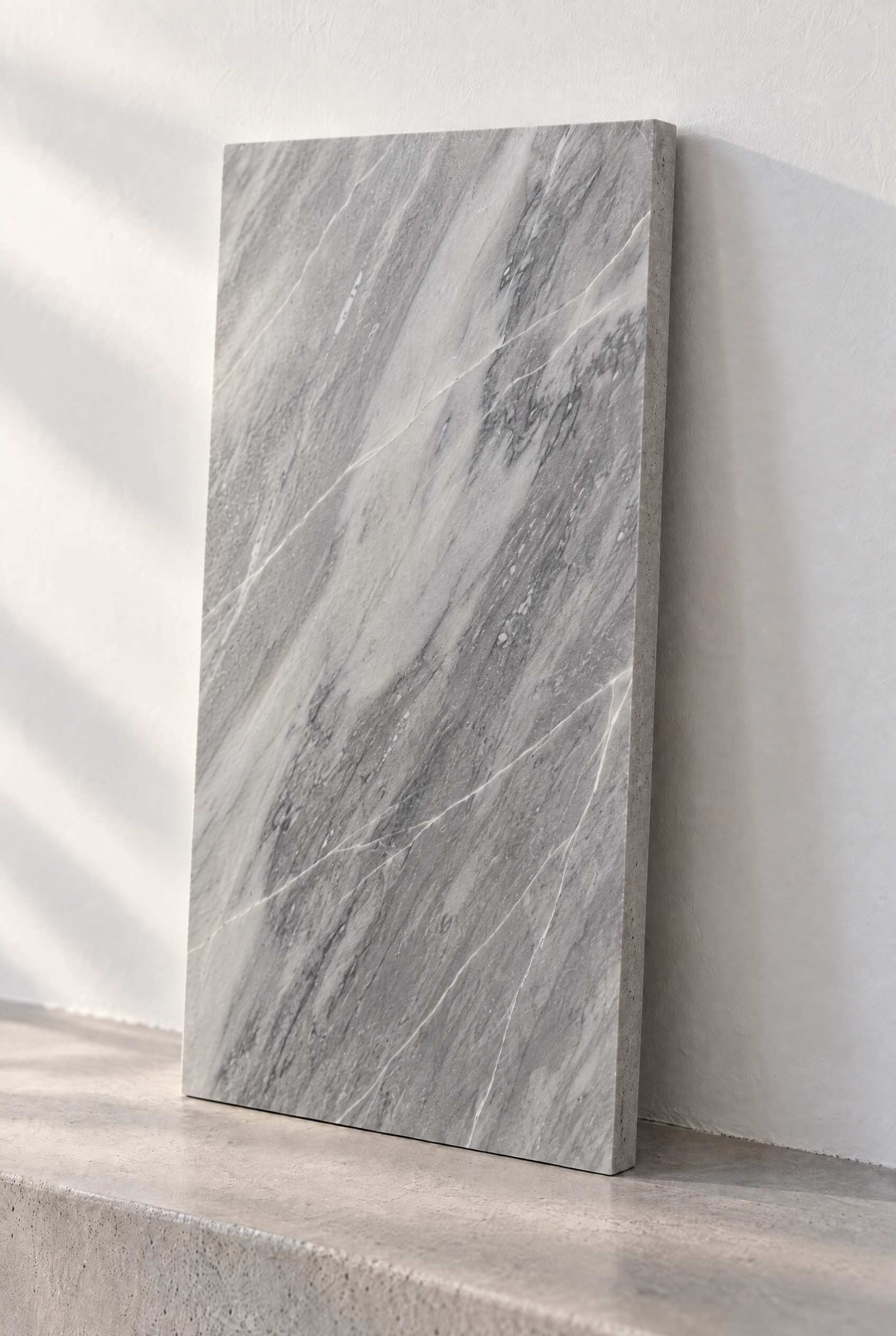 Illustration of a honed marble tile in Atlantic Gray, leaning against a white wall on a concrete step.