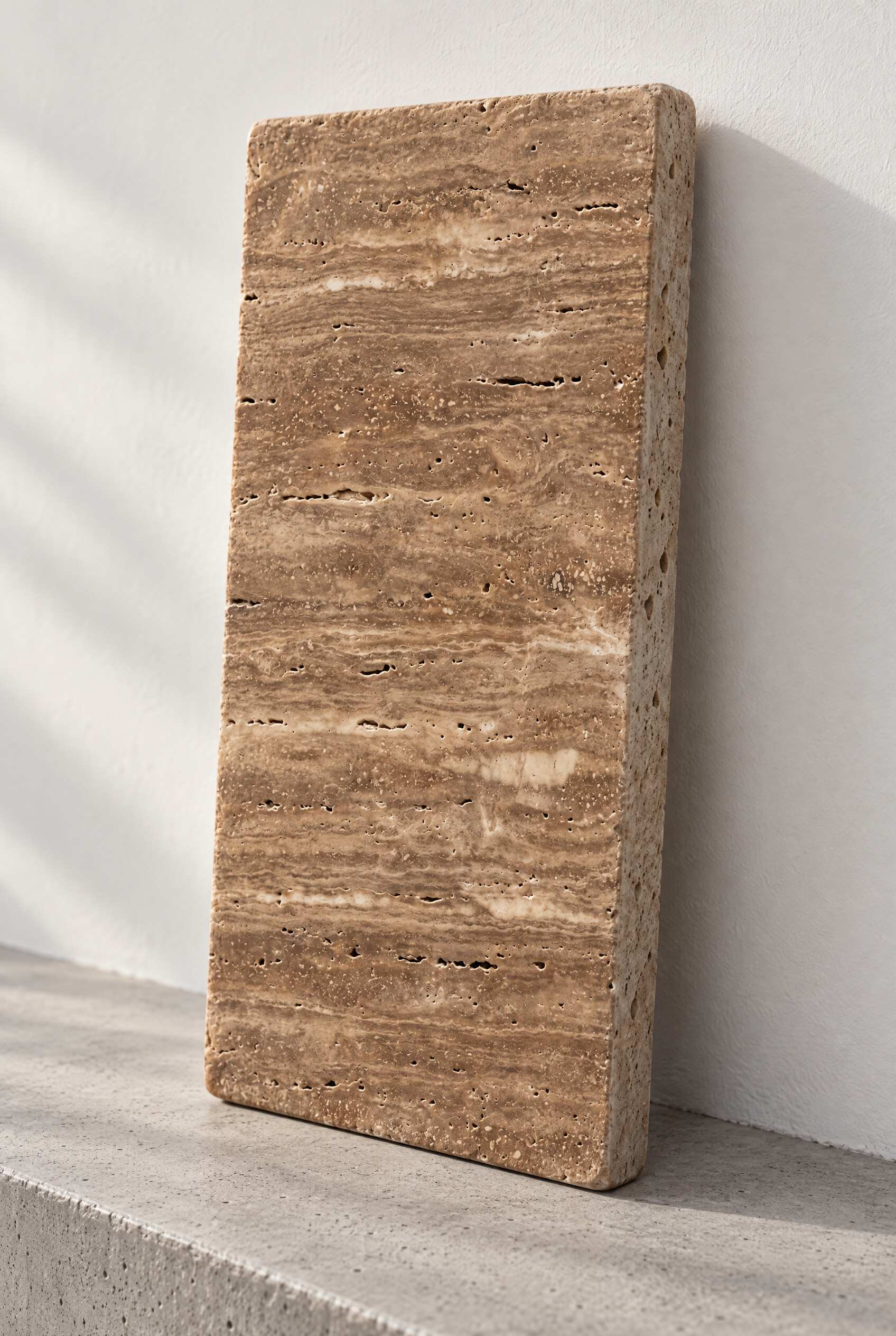 Illustration of a tumbled travertine paver in Noce, leaning against a white wall on a concrete step.